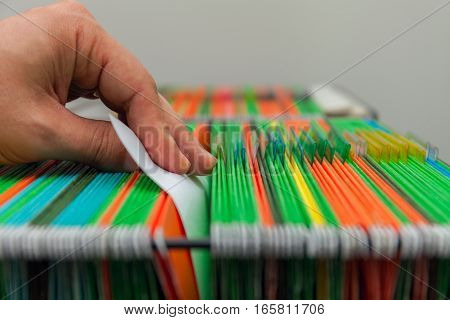 Abstract background of colorful hanging file folders in drawer. Mans hand. Stock photo