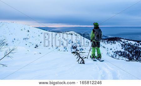 Young man on splitboard on the mountain ridge in evening light looking to horizon