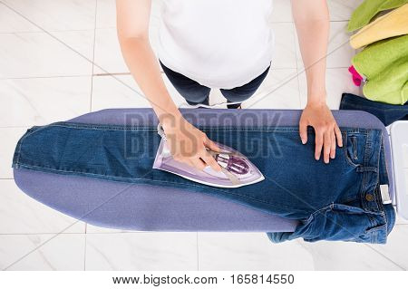 High Angle View Of Young Woman Ironing Jeans On Ironing Board At Home