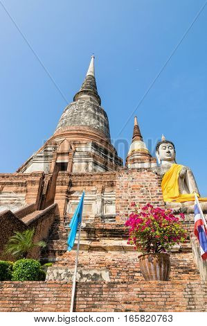 Buddha statue at the bottom of a large ancient pagoda on blue sky background at Wat Yai Chai Mongkon temple in Phra Nakhon Si Ayutthaya Historical Park Ayutthaya Province Thailand