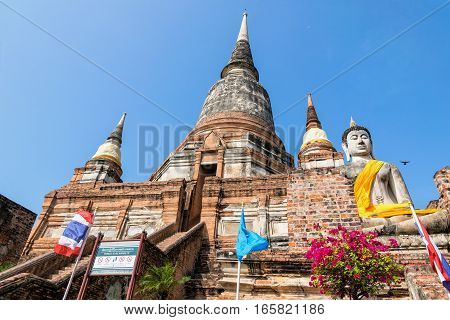 Buddha statue at the bottom of a large ancient pagoda on blue sky background at Wat Yai Chai Mongkon temple in Phra Nakhon Si Ayutthaya Historical Park Ayutthaya Province Thailand