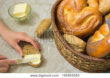 Woman spread the butter on the slice of bread and different bread in the wicker basket