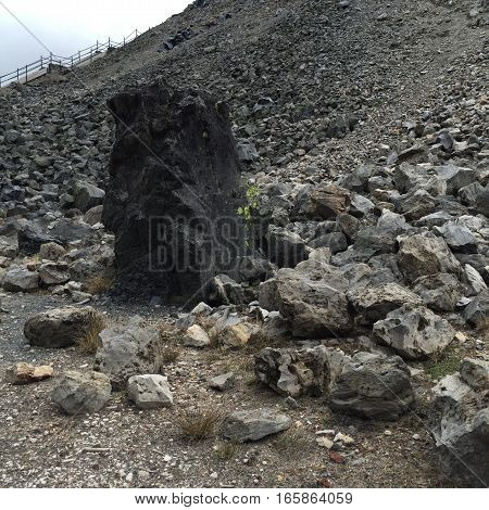 An obsidian boulder towers above the rocks on a hill with a trail that's accessed by stairs at the Big Obsidian Flow part of the Newberry National Volcanic Monument in Central Oregon.