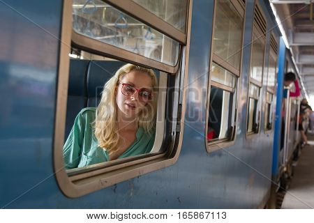 Blonde caucasian woman looking trough old retro blue train window , traveling by train in third world country.