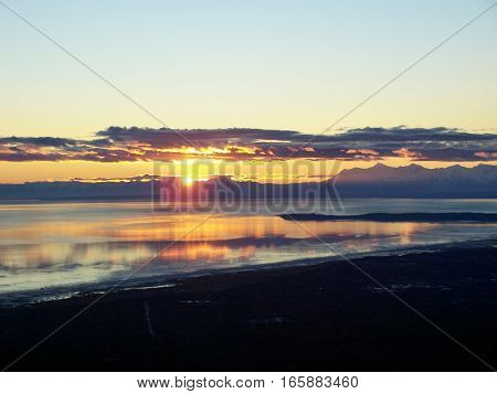 Amazing view of sunset or sunrise reflecting in the ocean from the top of mountain in Anchorage Alaska. Land silhouetted against a colorful morning or evening sky.