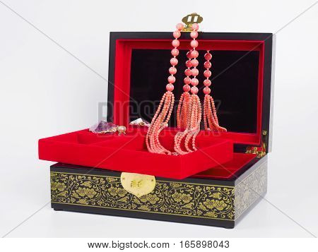 Picture of the opened jewel-box with red fit-out. Wooden jewel-box with pink coral bead necklace on white background. Side view.