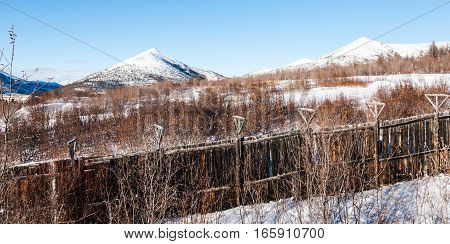 Old prison wooden fence with barbed wire on mountain background