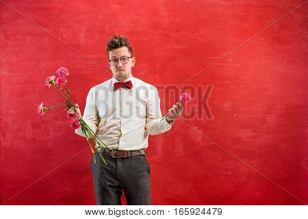 The young funny man with broken bouquet on red studio background. Concept - unhappy love