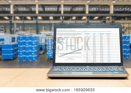 Laptop with analysis screen on table with blur warehouse cargo in factory. Smart factory concept.