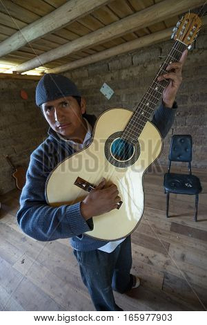 July 22 2016 San Bartolome Ecuador: an indigenous luthier holds up an finished guitar in his small rural shop