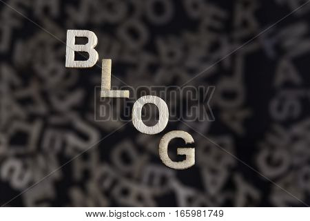 Blog wooden letters text on an angle created in wood floating above random letters below out of focus on a black background