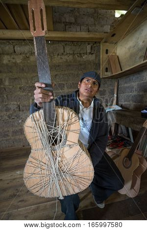 July 22, 2016 San Bartolome, Ecuador: an indigenous luthier holds up an unfinished guitar in his small rural shop