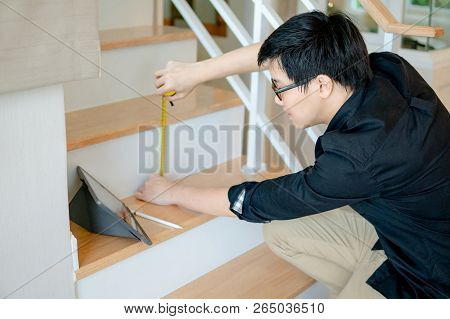 Young Asian Worker Using Tape Measure For Measuring Riser And Thread On Stair In The House. Writing 