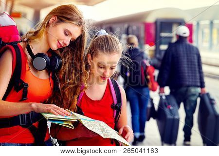 Traveller girl female wear headphones with backpack and tourism outfit paper map at railway station city outdoor. Terminal train locomotive and people with suitcase on background.