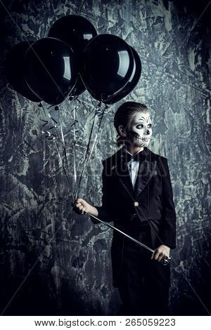 Portrait of a child boy with carnival make-up of a skeleton wearing elegant tail-coat. Studio shot over dark grunge background. Halloween. Dia de los muertos. The Day of the Dead.