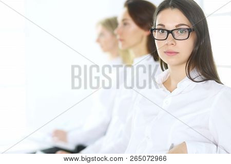 Attractive Businesswoman At Meeting Or Conference Against The Background Of Colleagues. Group Of Bus