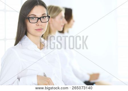 Attractive Businesswoman At Meeting Or Conference Against The Background Of Colleagues. Group Of Bus