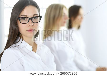 Attractive Businesswoman At Meeting Or Conference Against The Background Of Colleagues. Group Of Bus