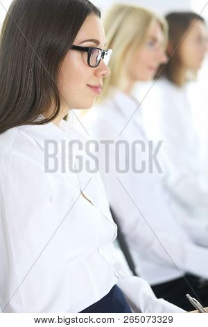Attractive Businesswoman At Meeting Or Conference Against The Background Of Colleagues. Group Of Bus