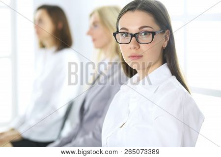 Attractive Businesswoman At Meeting Or Conference Against The Background Of Colleagues. Group Of Bus