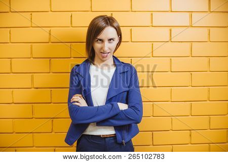 Beautiful Cheerful Modern Crazy Blonde Girl Showed Her Tongue Against Yellow Brick Wall. Sidelong Gl