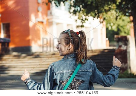 Cheerful Little Girl In Jeans Clothes With Star On Her Back Against Blurred City Landscape.