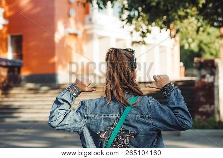 Cheerful Little Girl In Jeans Clothes With Star On Her Back Against Blurred City Landscape.