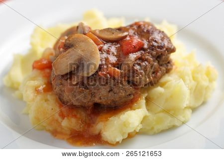 Salisbury steak with mashed potato under tomato and mushroom gravy