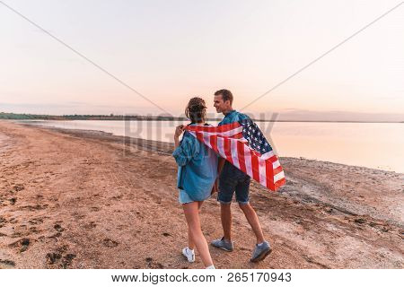 American Couple Covered In American Flag Walking On Beach