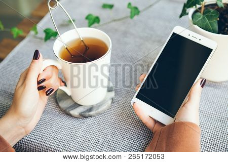 Young Woman Is Drinking Tea And Reading Popular Blogs, Commenting Photos, Liking Posts And Videos. C