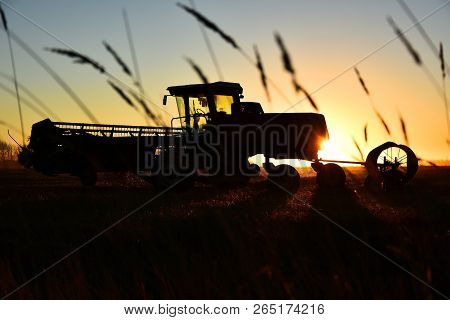 A Silhouette Image Of Old Agricultural Equipment In A Filed At Sunset.