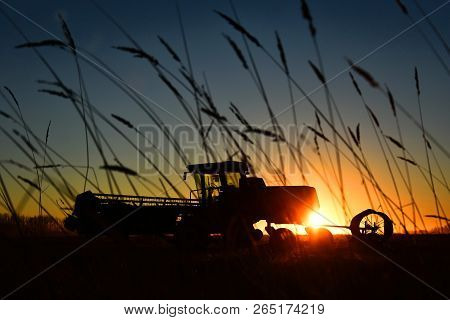 A Silhouette Image Of Old Agricultural Equipment In A Filed At Sunset.