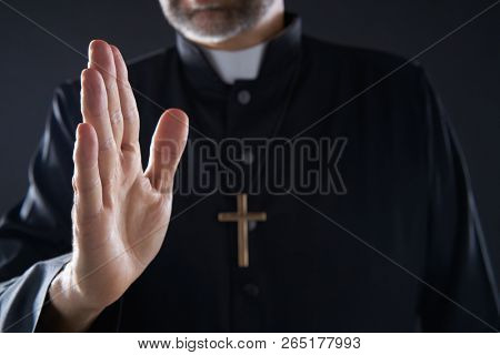 Pirest hand blessing closeup with cross and clergyman background