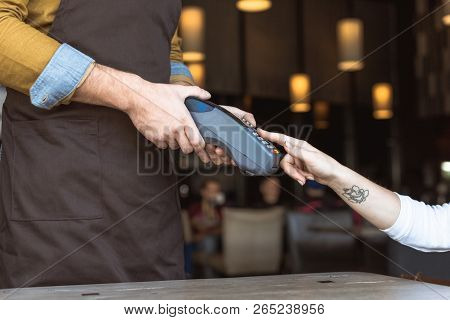 Cropped Shot Of Waiter Holding Payment Terminal While Female Client Entering Pin In Cafe