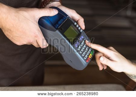 Cropped Shot Of Waiter Holding Payment Terminal While Customer Entering Pin In Cafe