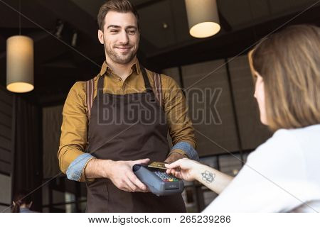 Happy Young Waiter Holding Payment Terminal While Client Doing Contactless Purchase With Credit Card
