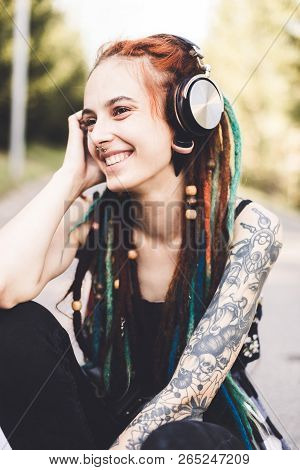 Young Girl With Tattoo And Dreadlocks Listening To Music In The Park