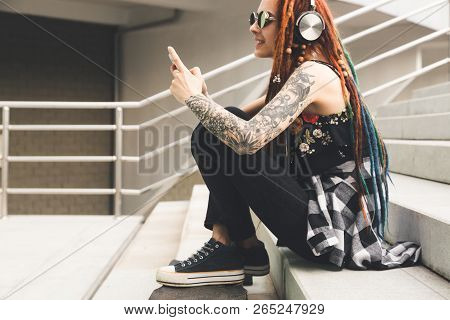 Young Girl With Tattoo And Dreadlocks Listening To Music While Sitting On The Steps