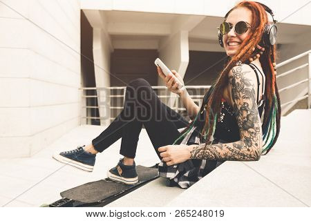 Young Girl With Tattoo And Dreadlocks Listening To Music While Sitting On The Steps