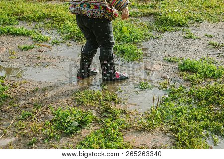 Little Girl In Boots Trampling A Muddy Puddle In Autumn