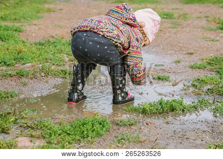 Little Girl In Boots Trampling A Muddy Puddle In Autumn