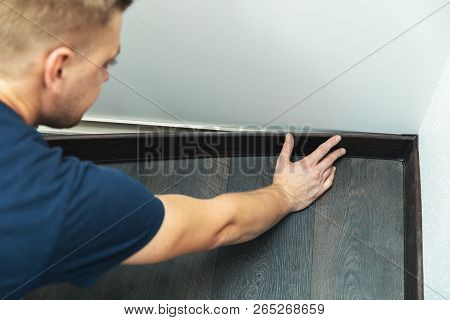 Worker Installing Plastic Baseboard On The Laminate Floor