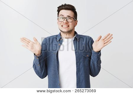 Sorry I Messed Up. Guilty Young And Handsome Male In Glasses And Blue Shirt Raising Hands Near Shoul