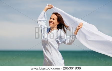 people and leisure concept - happy woman with shawl waving in wind on summer beach