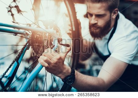 Handsome Bike Mechanic Repairs Bicycle In Workshop. Closeup Portrait Of Young Bearded Man Wearing Wh