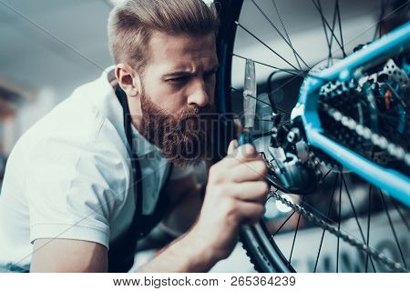 Bike Mechanic Repairs Bicycle In Workshop. Closeup Portrait Of Young Caucasian Man Wearing Apron Exa