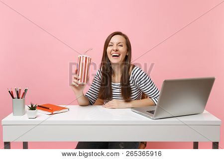Young Laughing Woman Holding Plactic Cup With Cola Or Soda Sit And Work At White Desk With Contempor