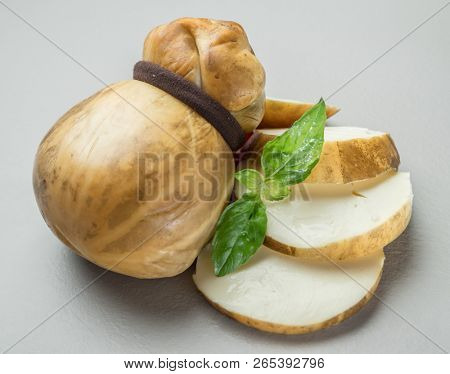 Traditional Italian smoked Scamorza cheese with herbs on gray background.