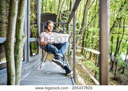 Poortrait Of A Handsome Man Working With Laptop On The Balcony Of The House In The Beautiful Green F