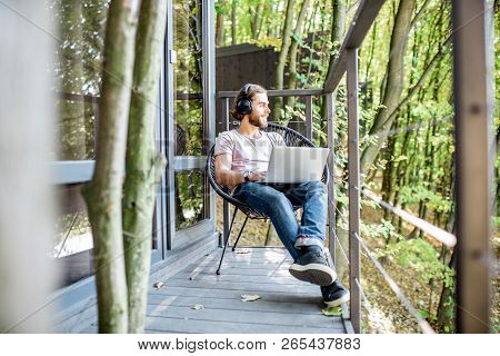 Poortrait Of A Handsome Man Working With Laptop On The Balcony Of The House In The Beautiful Green F